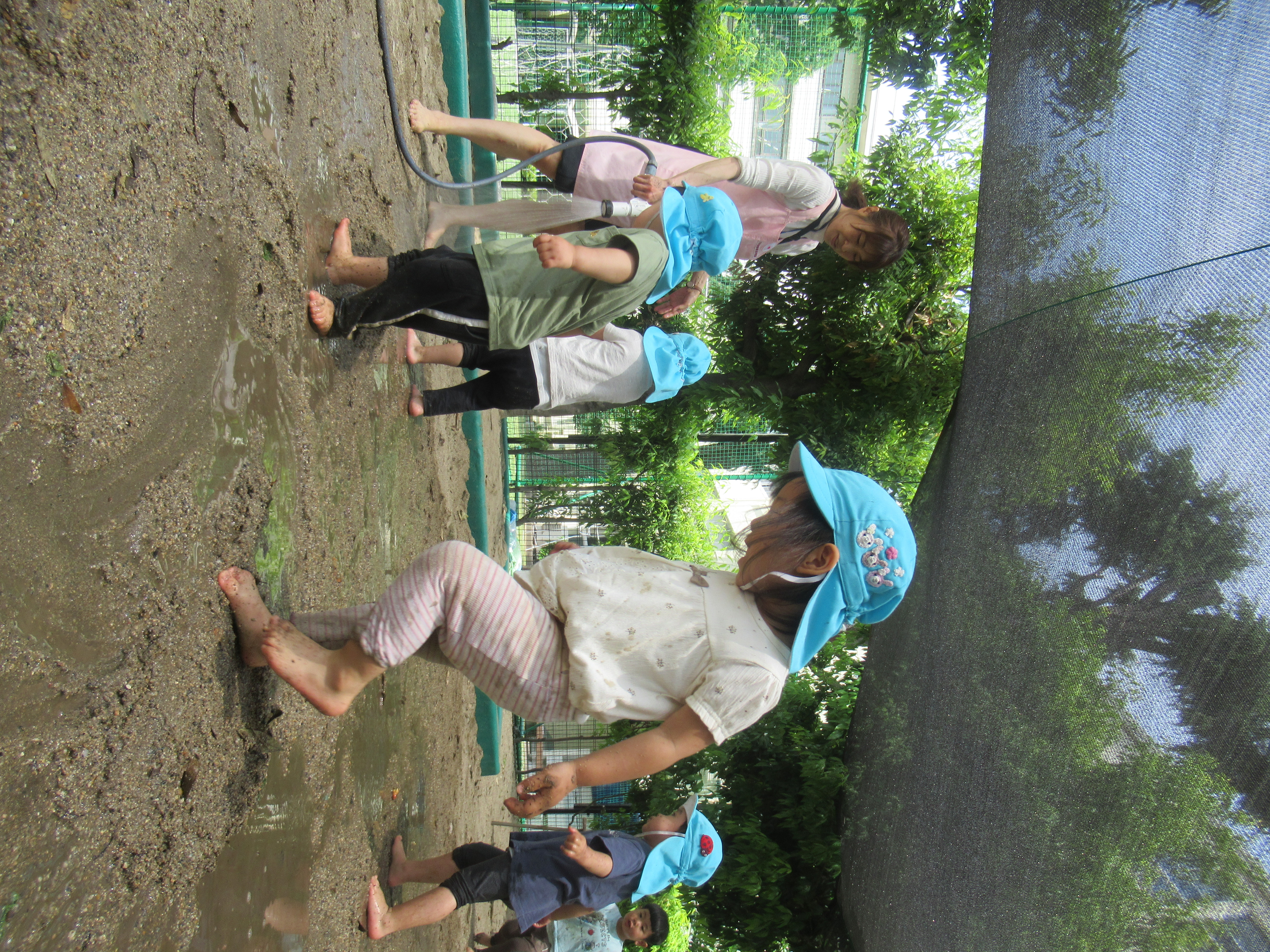 水を撒く保育者と園児たち