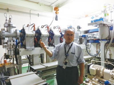京都大学複合原子力科学研究所内にある世界初のBNCT治療(治験)を実施した加速器の前で解説する鈴木実教授。一つの部屋に入るサイズで、今後病院での運用を可能とする画期的な進歩。