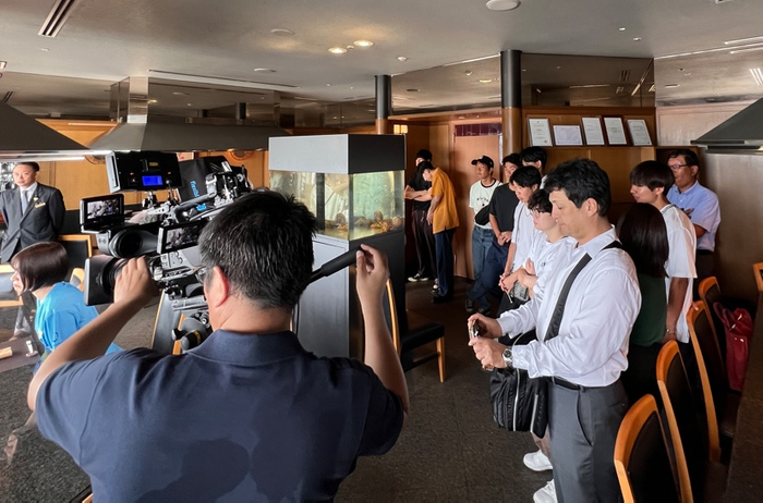 テレビの撮影風景を見学するラボの学生たち＝ホテルグランヴィア岡山で