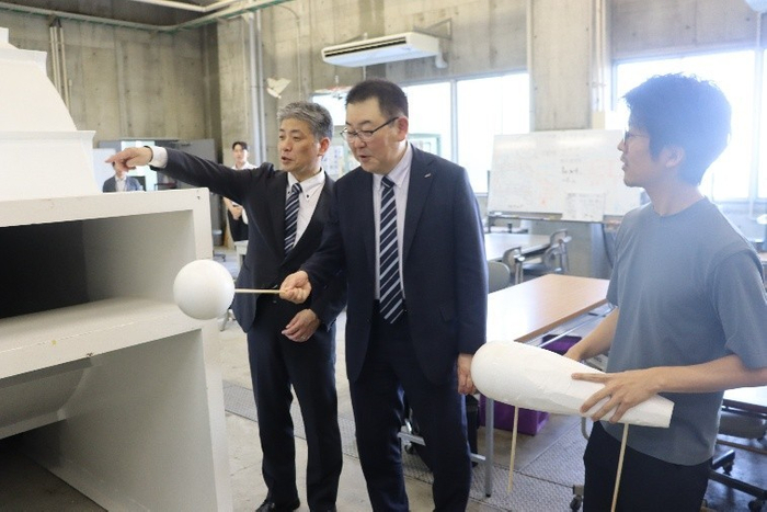 風洞実験装置を試してみる烏田社長（中央）ら。右は機械システム工学科の岩野耕司准教授