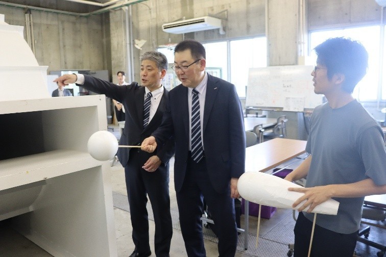 風洞実験装置を試してみる烏田社長(中央)ら。右は機械システム工学科の岩野耕司准教授